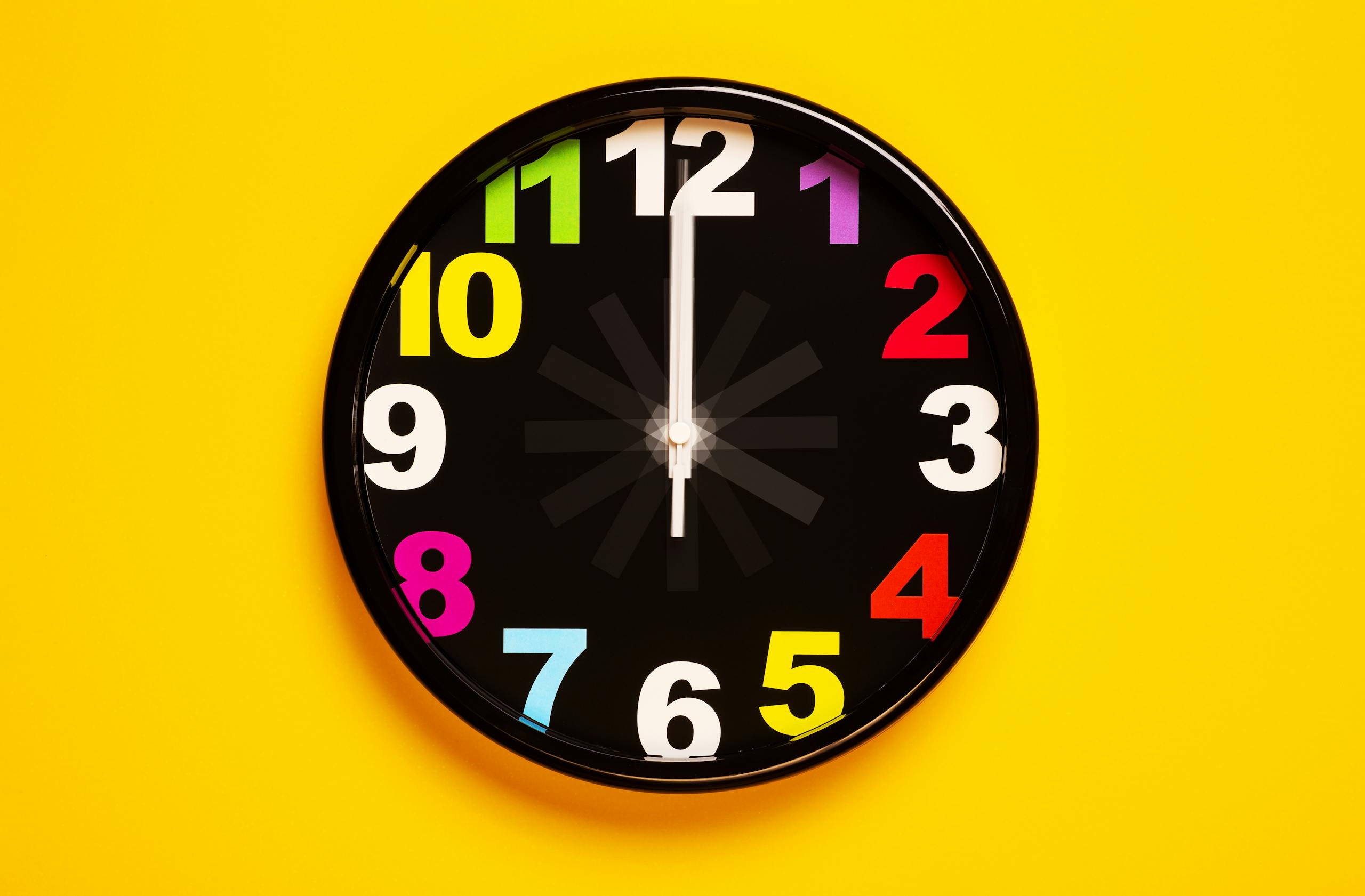 Vibrant wall clock with colorful numbers on a bright yellow background, emphasizing modern decor.
