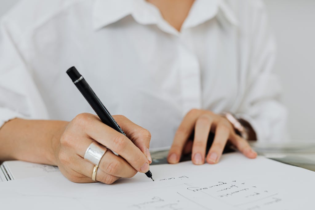 A detailed close-up of hands writing in a notebook with a black pen.