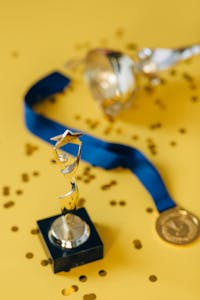 Close-up of a golden trophy and medal on a yellow confetti-strewn surface.