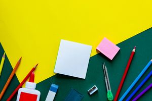 A vibrant flat lay of various school supplies on a yellow and green geometric background.